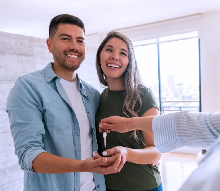 Smiling couple receiving house keys from a real estate agent in a bright, modern apartment.