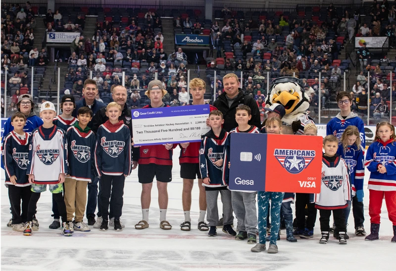 Group on ice holding donation check and debit card at Tri-City Americans game.