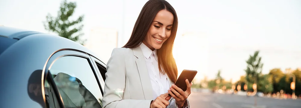 Woman standing by a car and using her smartphone outdoors.