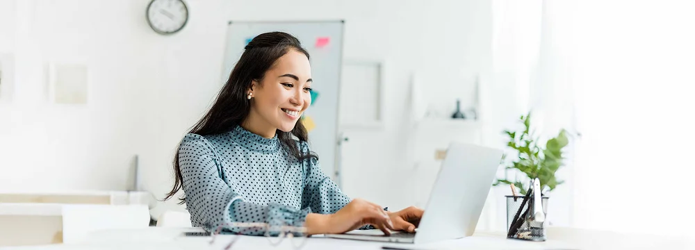 Woman smiling while working on a laptop at a desk.