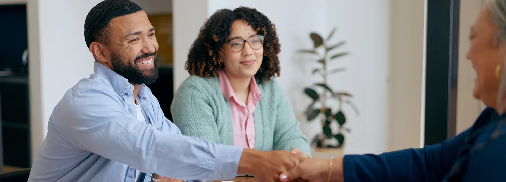 Two people smiling and shaking hands during a loan approval.